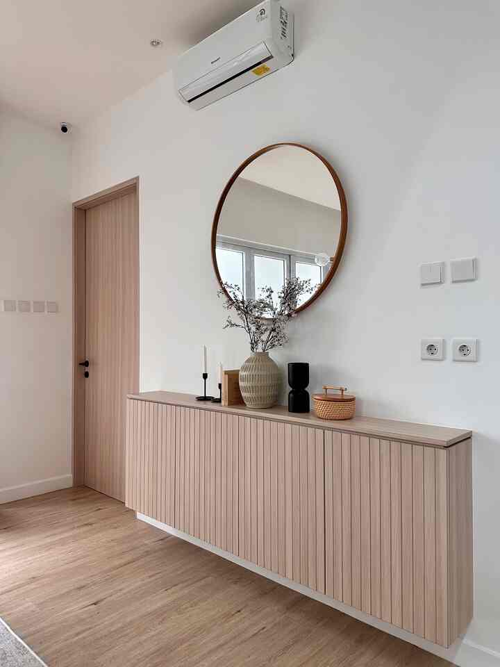 Wood tone and white entrance space featuring a round mirror and floating cabinet creating a clean atmosphere.