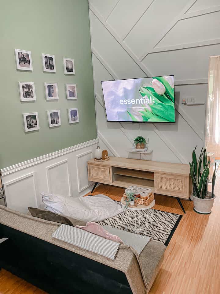 Natural-toned living room with green accent wall, featuring wooden TV stand and fabric sofa creating a cozy atmosphere.