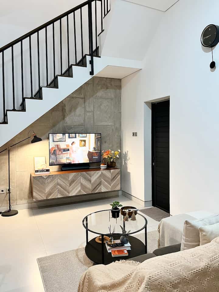 Modern living room in black and beige tones featuring metal staircase, TV stand, and sofa with a cozy atmosphere