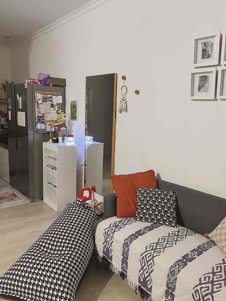 A compact living room with white walls and a gray sofa, featuring cushions and patterned textiles creating a cozy atmosphere