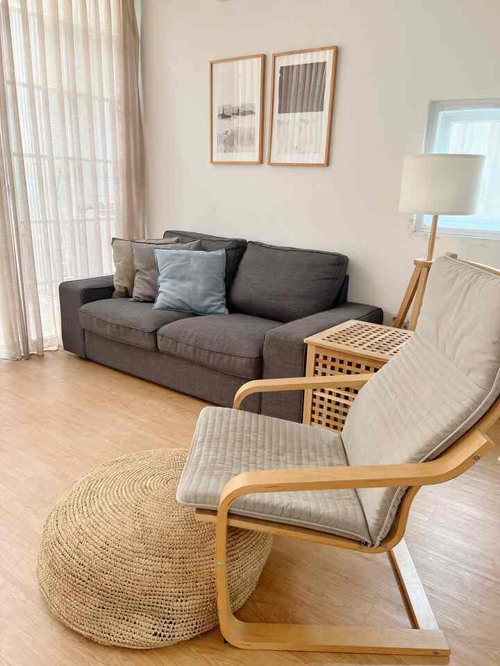 Bright wood-tone floor and minimalist modern living room featuring gray sofa and light gray armchair in simple setting