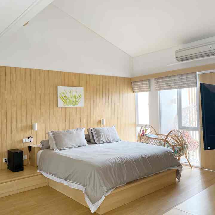 Wood tone and white bedroom featuring a large central bed, wood paneled wall, and balcony windows creating a cozy atmosphere