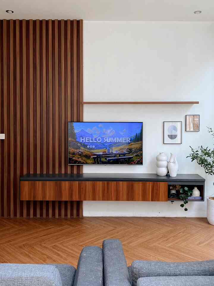 Modern living room with white walls and brown wood tone furniture, featuring a wall-mounted TV and sleek floating TV stand in a clean design space