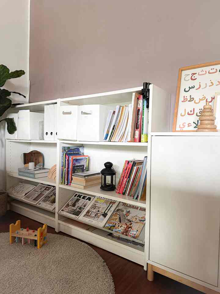 Clean Nordic kids' nook featuring white corner storage units, bookshelves, and a beige rug with harmonious wood tones