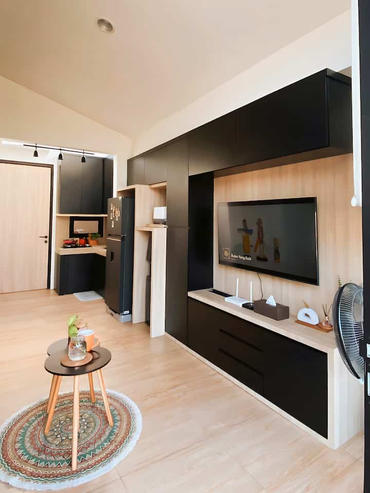 Modern living room and kitchen with wood tone floors and walls complemented by black furniture