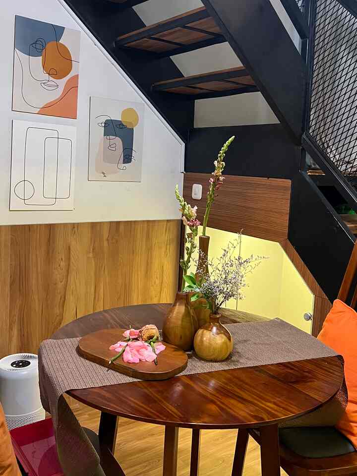 Warm brown wood tones with black staircase in a compact dining room featuring a round dining table with floral vases and abstract wall art