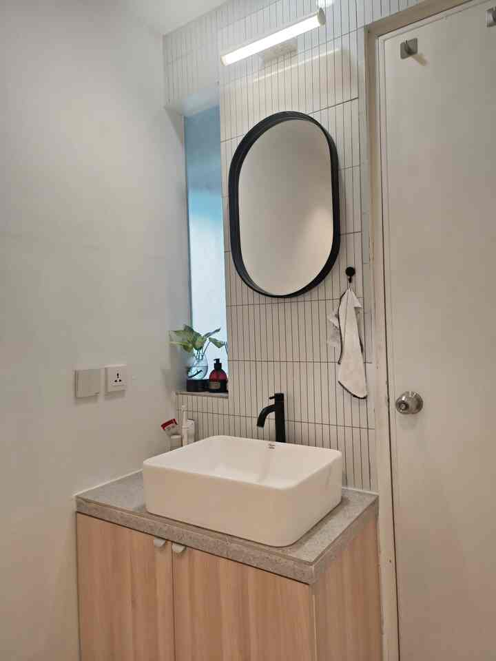 Monotone bathroom space featuring custom cabinet and black-framed mirror with simple, warm atmosphere