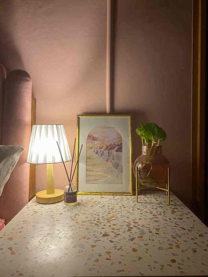 Bedroom space with pink wall and terrazzo table, featuring gold picture frame and table lamp in Art Deco style interior