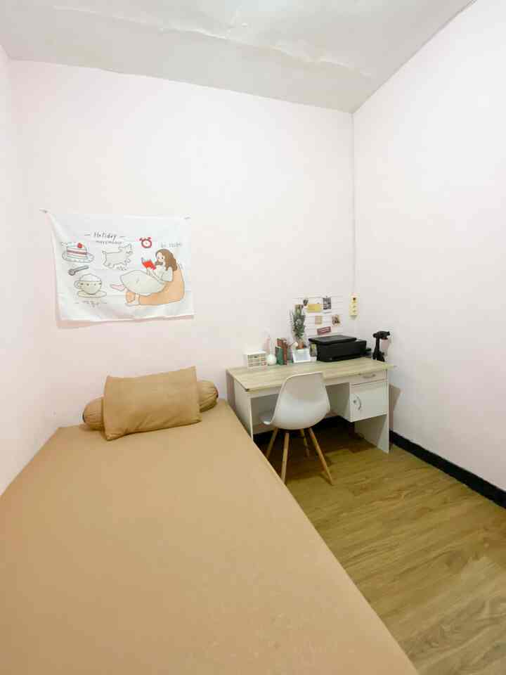 Light pink walls and beige bedding in a studio bedroom featuring a desk and chair in a simple layout