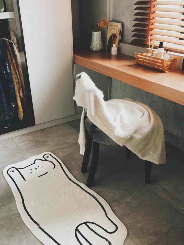 Small walk-in closet with gray tiled floor and brown wooden desk, featuring a cute cat-shaped carpet and black stool chair