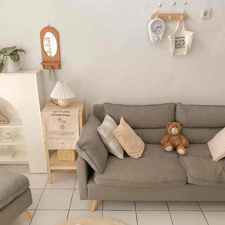 Compact living room with white walls and brown wood tones, featuring gray sofa with cushions and table lamp for cozy atmosphere