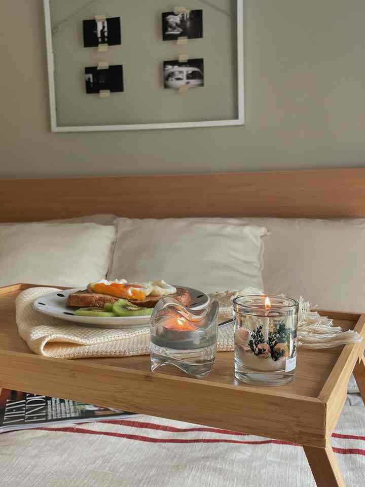 Warm natural-toned bedroom with a wooden tray holding breakfast and lit candles creating a cozy atmosphere