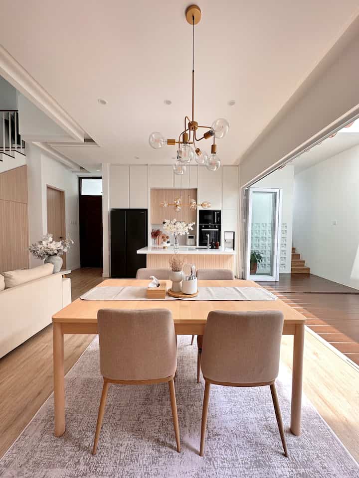 Bright natural modern dining and living space featuring wood-tone dining table, sofa, and white walls, creating a clean atmosphere