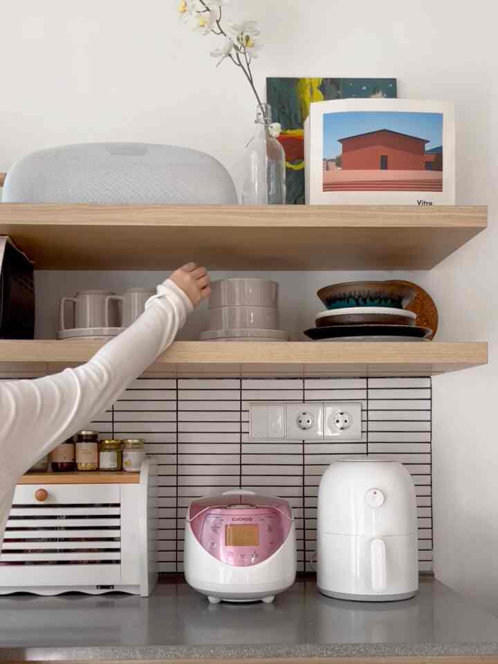White and wood tone kitchen with organized diningware including bowls and cups on wooden shelves, featuring a clean and minimalistic atmosphere