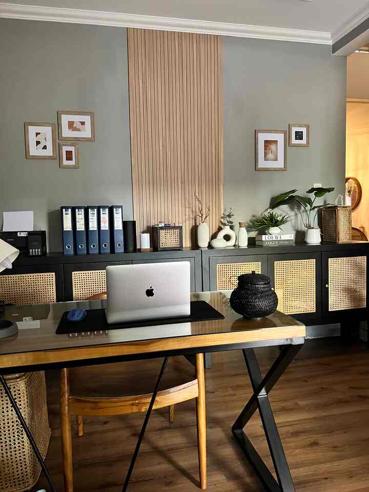 Gray-walled home office workspace with wood-tone flooring, featuring a glass-top desk and rattan furniture in vintage style