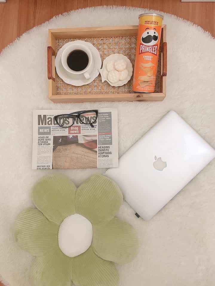 Simple and cozy compact space on white rug featuring lounge cushion, laptop, coffee, and snacks