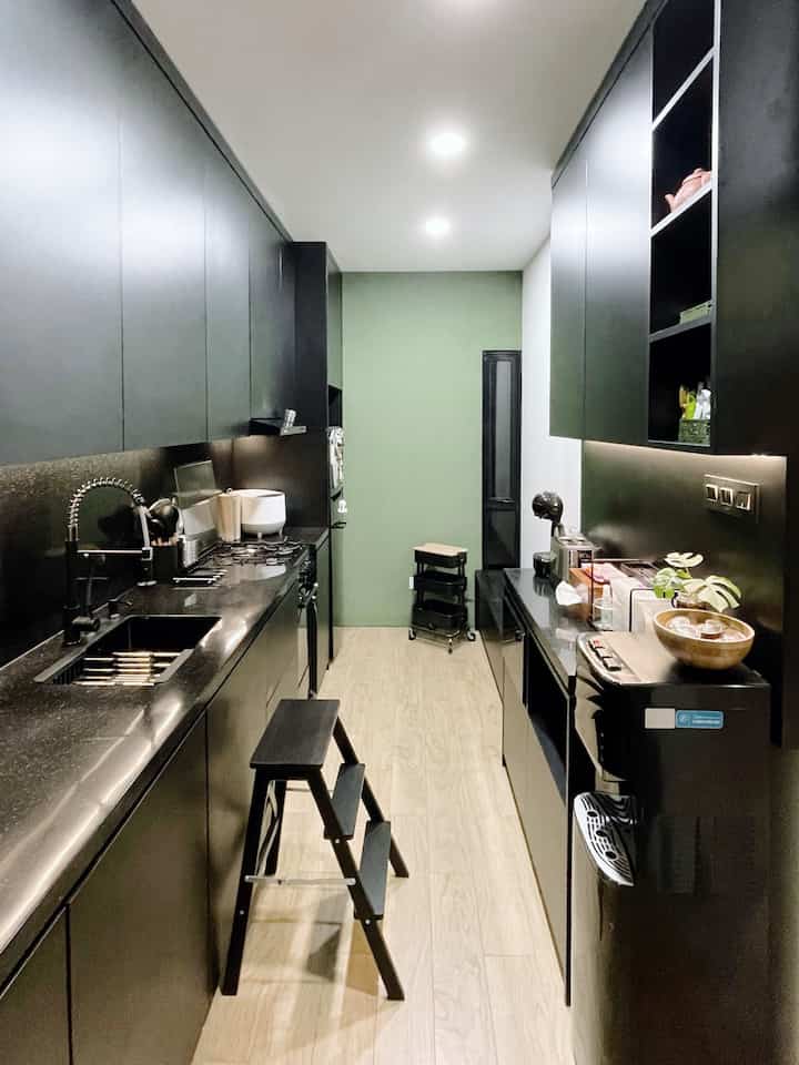 Modern compact kitchen space featuring black cabinets and a green accent wall creating a sleek, personalized atmosphere