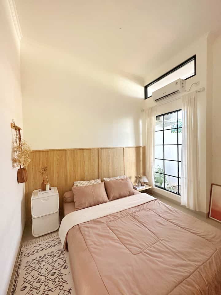 White and brown toned bedroom featuring bed and curtains in a small, simple, cozy space