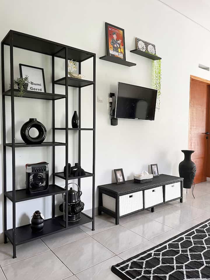 Monotone living room with white walls and black furniture, featuring a TV and storage cabinet in a simple and minimal setting