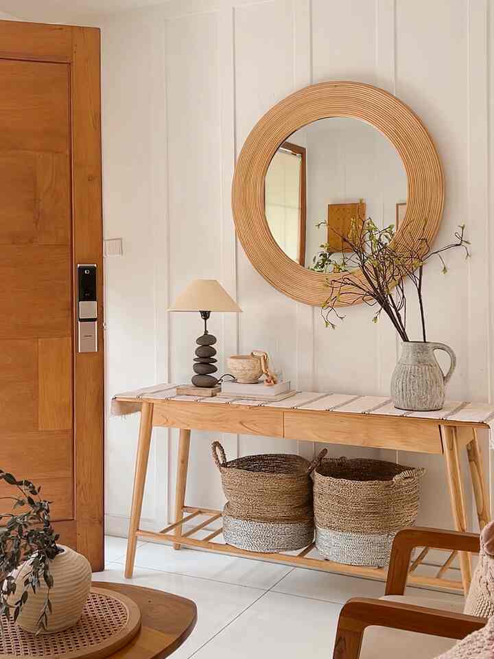 Natural tone entrance with wooden console table, round mirror, and rattan storage baskets in a simple setting