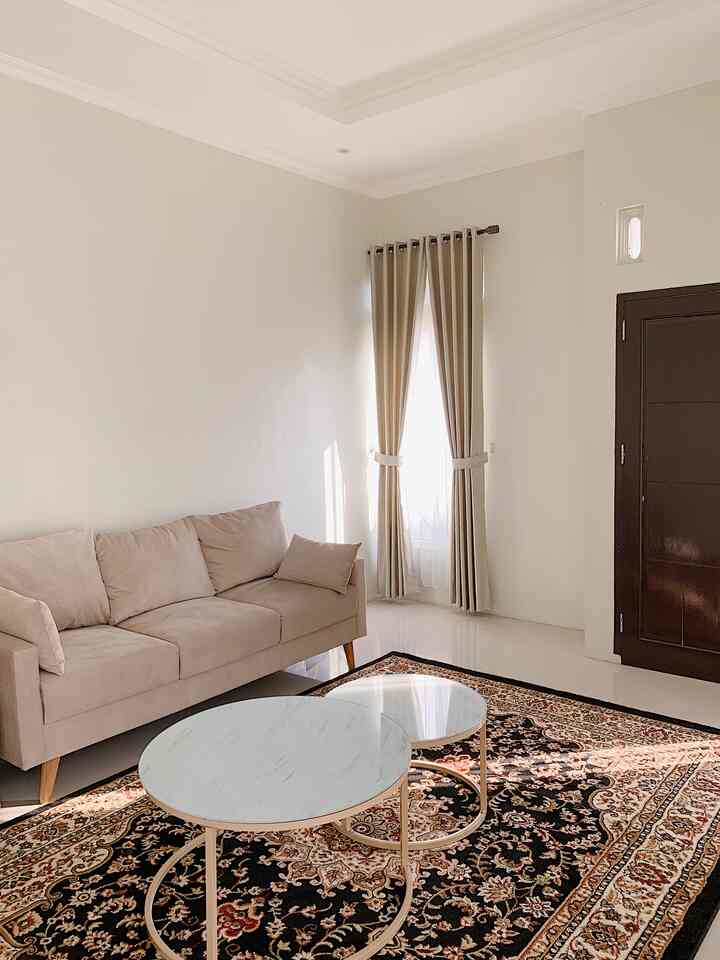 Beige-toned living room featuring a beige sofa, two round coffee tables, and a Turkish patterned carpet creating a minimal and cozy atmosphere