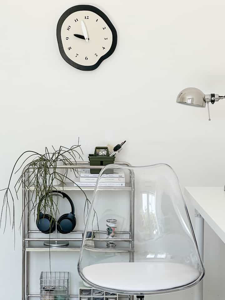 White and stainless steel toned minimalist home office featuring transparent chair and neat storage rack