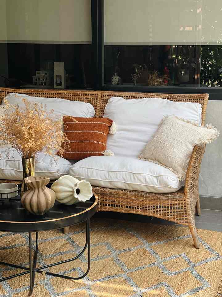 Natural color balcony space featuring a rattan sofa, brown tone carpet, and golden vases, creating a cozy cafe-style atmosphere