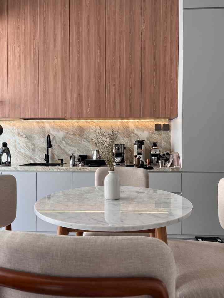 Modern minimalist kitchen and dining area featuring beige wood tones and a round marble dining table, sleek and clean atmosphere