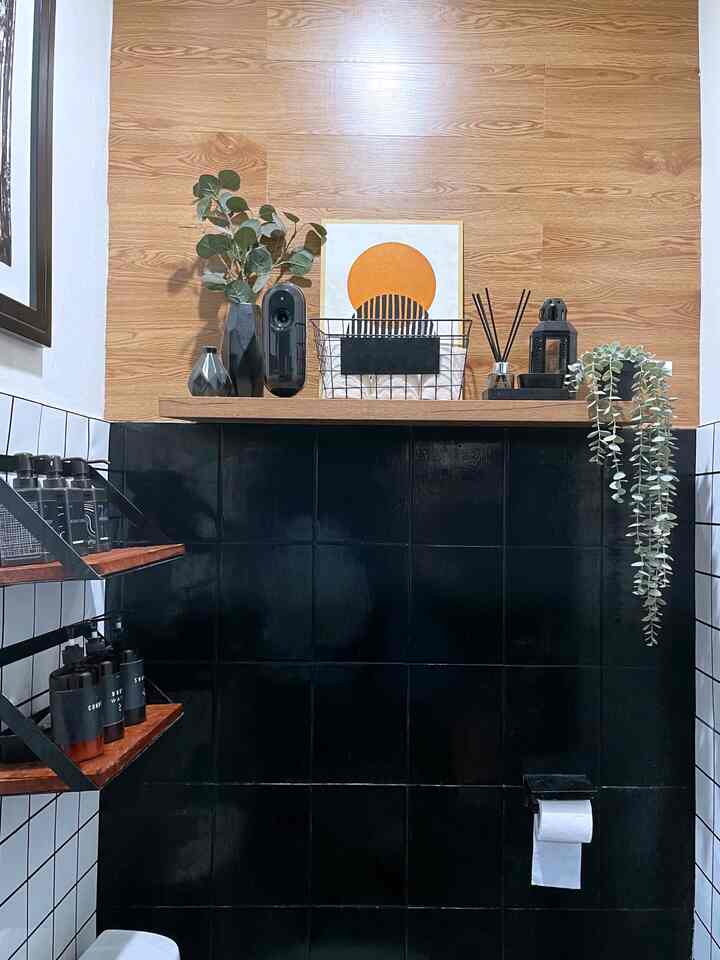 Modern small bathroom featuring black tiles, wood tone wall panels, shelves with decor and plants creating a cozy atmosphere