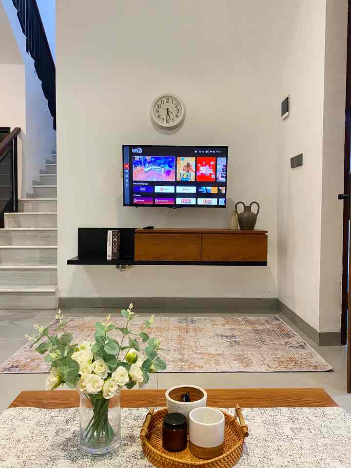 Living room with white walls and wood-tone furniture, featuring a central TV and clock creating a warm, cozy atmosphere