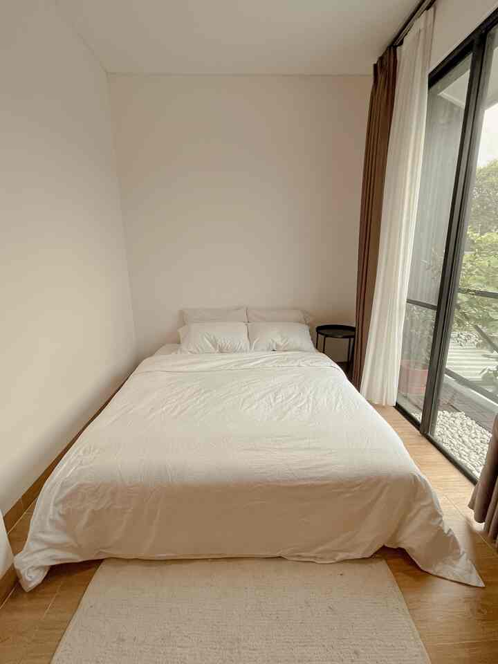 White and wood tone bedroom featuring large sliding window and simple side table with a cozy atmosphere