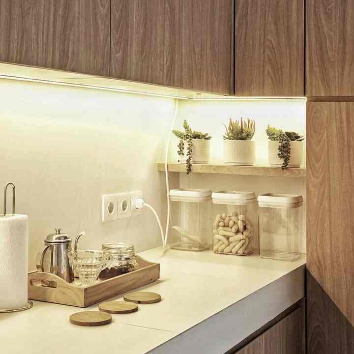 Minimalist kitchen featuring wood tone cabinets and white countertops, with coffee drip set and small plants on shelf