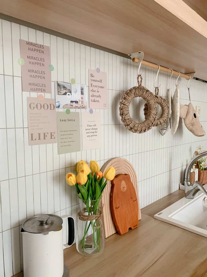 White tiled kitchen space with wood tone countertop, decorated with yellow tulips and mini posters, featuring cozy cafe style decor
