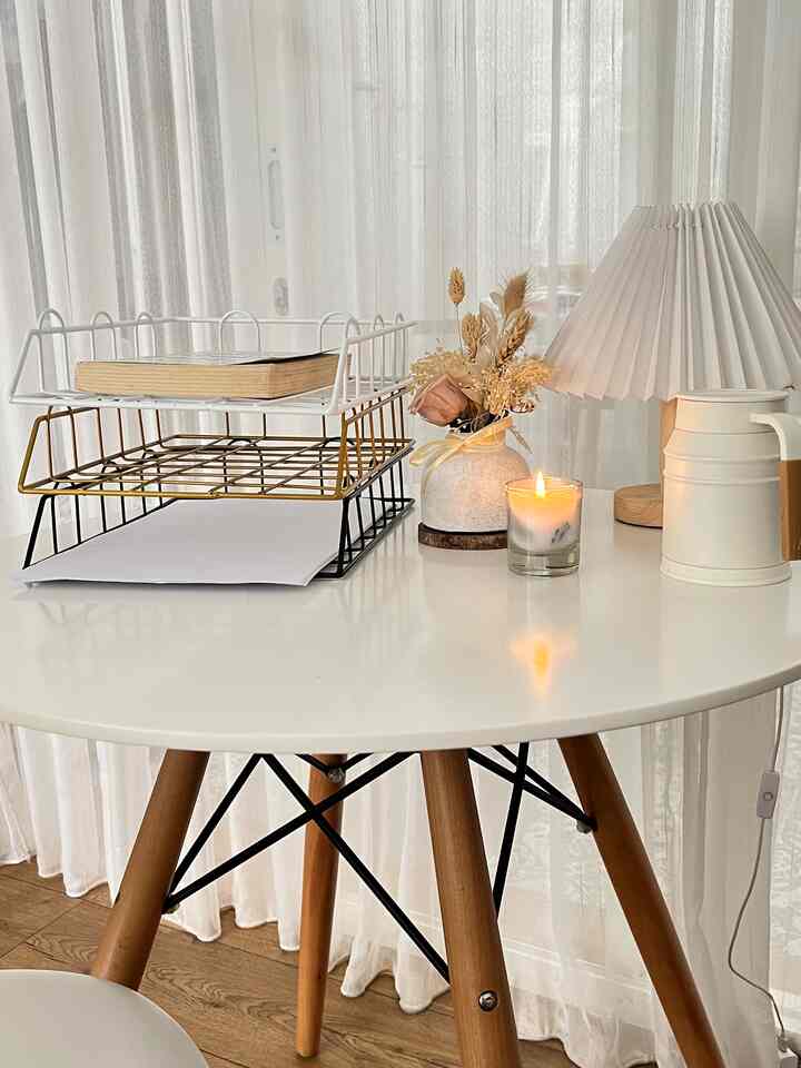 A white and wood tone home office featuring a tidy round desk with organized trays and table lamp, creating a cozy atmosphere