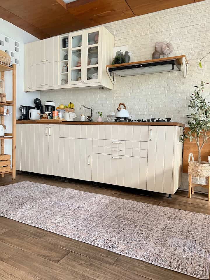 A cozy open kitchen and dining space featuring brown wood tones, white cabinetry, and a patterned carpet on warm wood flooring