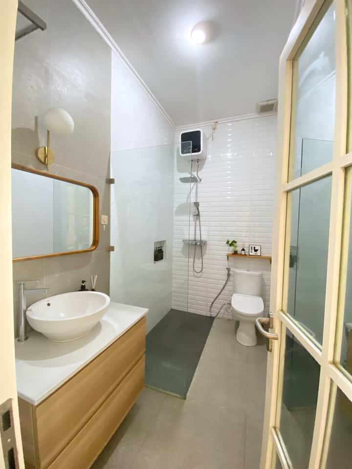 Modern bathroom with white and wood tones, compact long and narrow layout featuring a minimalist sink and shower area