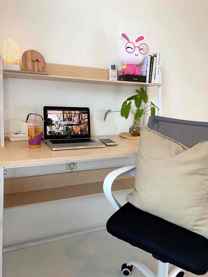 Modern simple home office with white walls and wood-tone desk, accented by pink bunny lamp and green plant for coziness