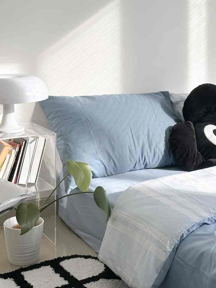 Bright bedroom with dominant white, blue, and black tones featuring an acrylic table and table lamp in a modern clean setting