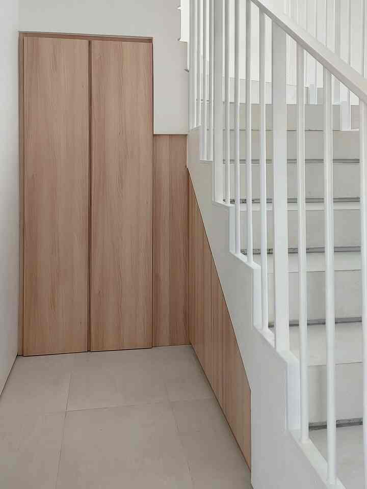 Minimalist storage space featuring wood-tone custom cabinets beside white stairs with vertical railings