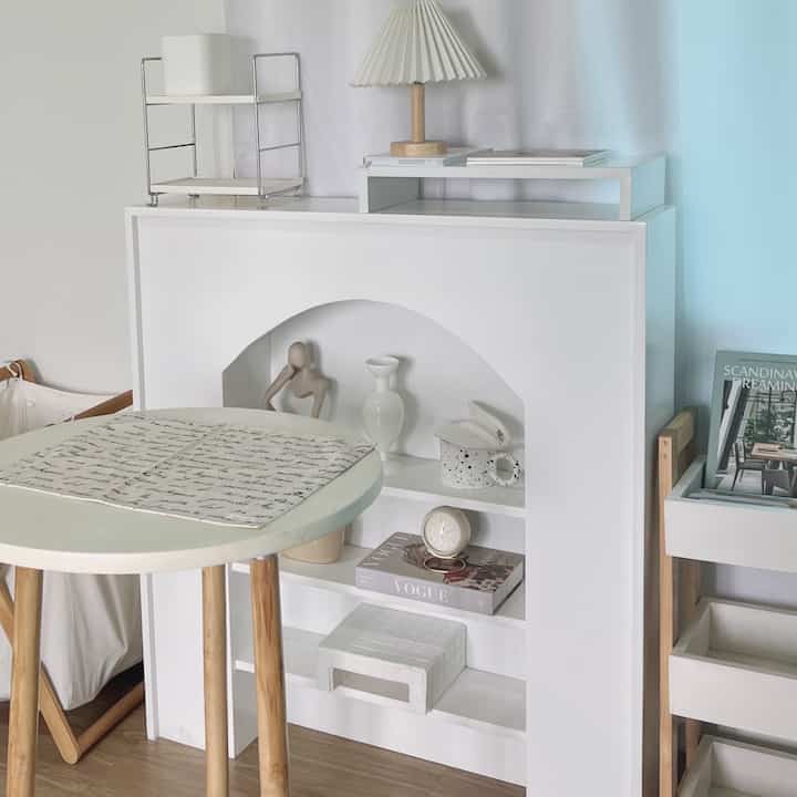 Simple multi-purpose space in white and wood tones, featuring an arched shelving unit and round table, creating a cozy home cafe atmosphere