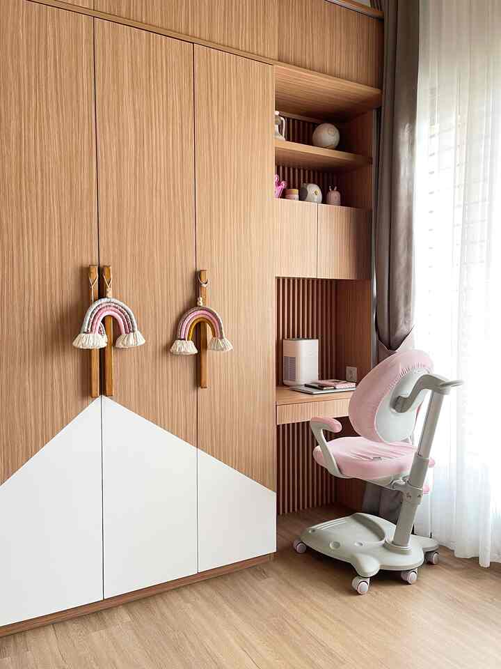 Wood tone and white kids' room featuring a large wardrobe and pink kids' desk chair in a neat setting