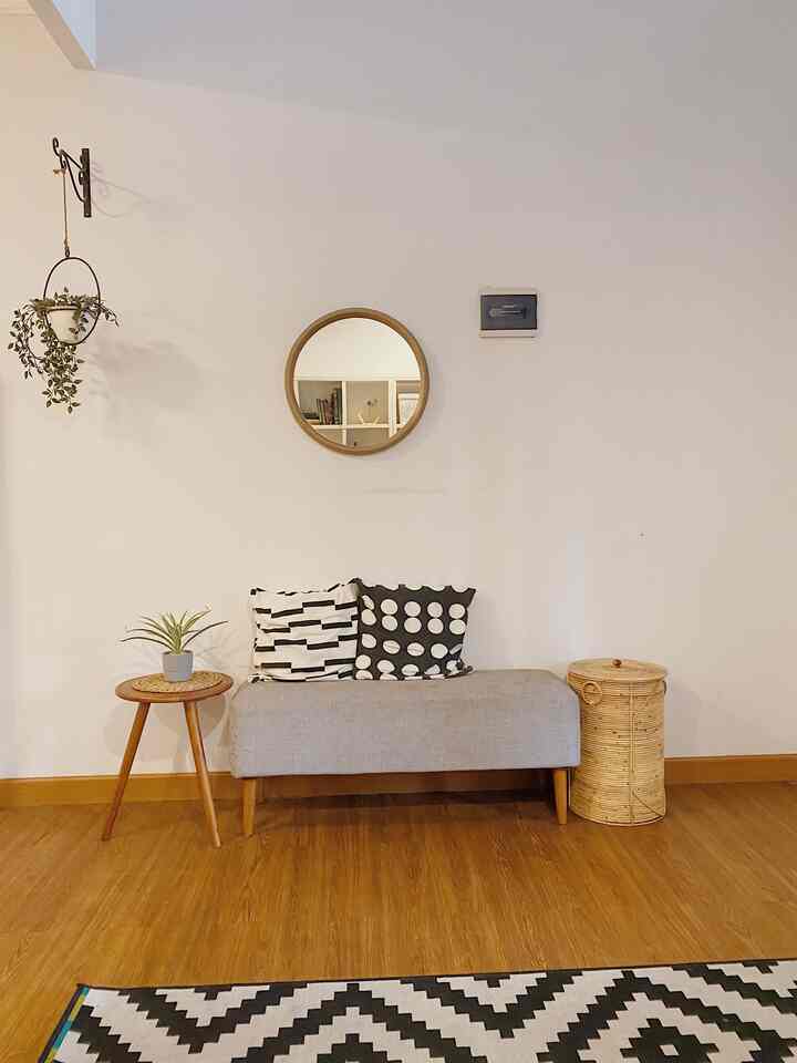 Natural color and wood tone living room entrance featuring a bench, round mirror, and plants with simple decor