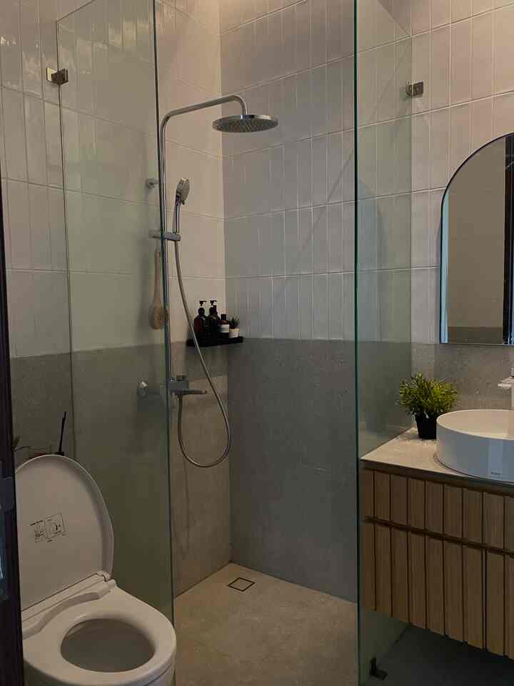 Compact bathroom with white tiled walls and light brown wooden cabinet featuring shower area, sink, and toilet in a minimalist setting