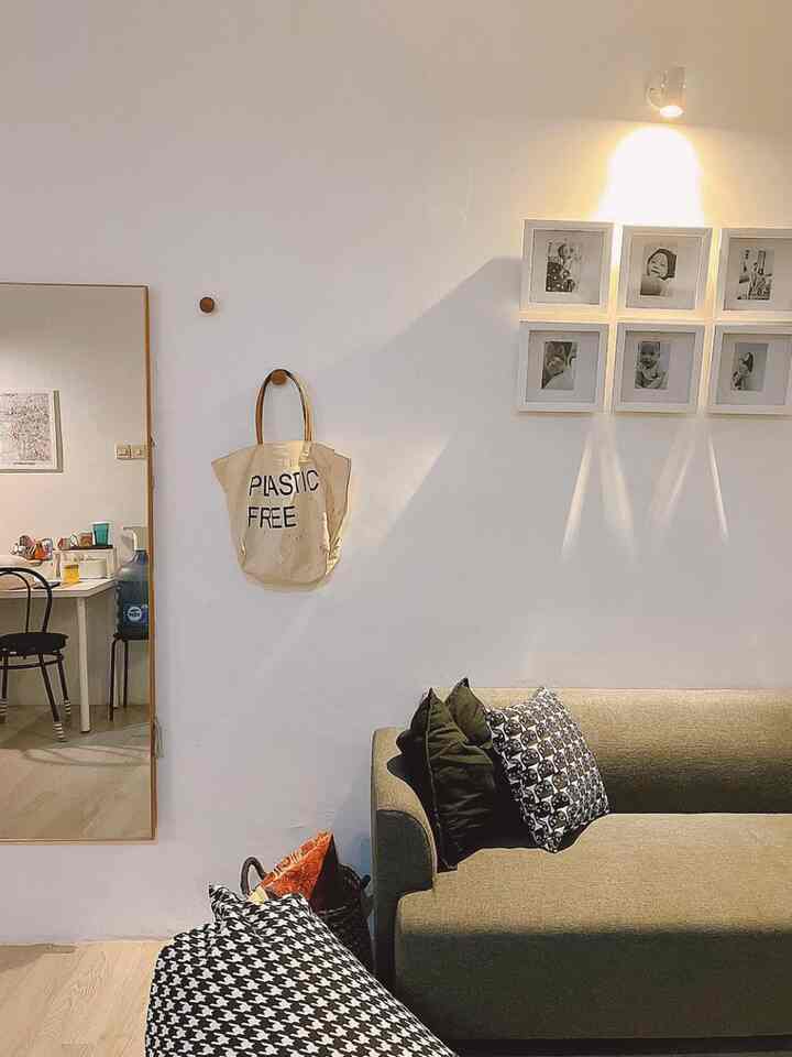 A white and brown toned living room featuring a clean sofa, cushions, and framed pictures on the wall creating a cozy and simple atmosphere