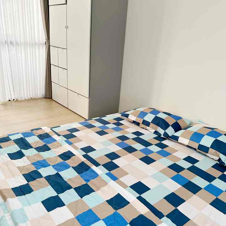 A white and wood-tone bedroom featuring a bed with patterned bedding in a tidy, minimalist space