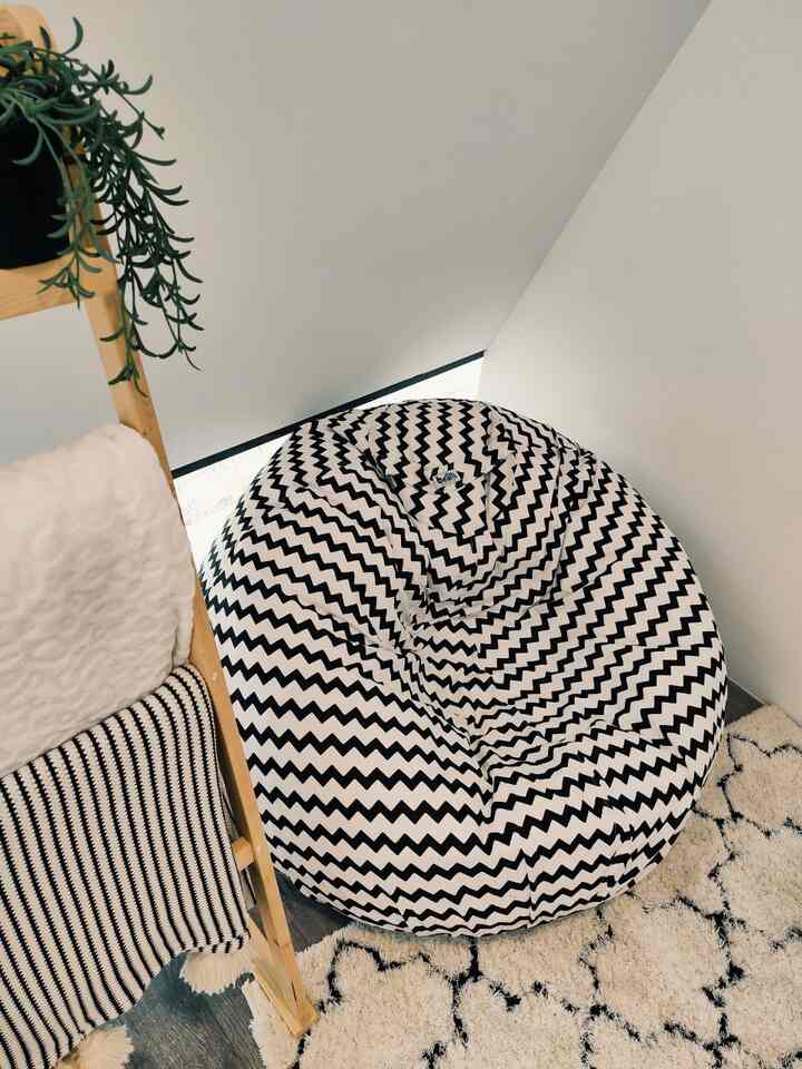 White and black corner of a small room featuring a zigzag patterned bean bag and wooden ladder shelf with a natural vibe