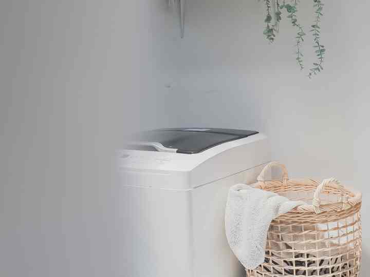 White and natural brown toned laundry room featuring a washing machine and rattan laundry basket with a clean atmosphere