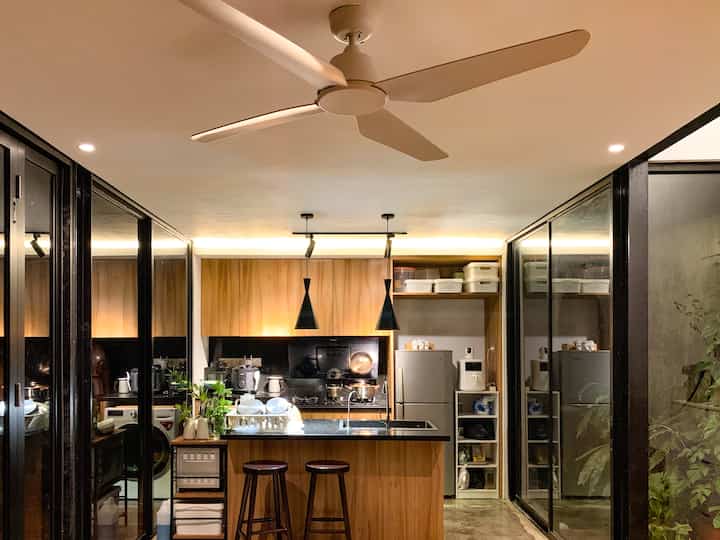 Modern kitchen space featuring warm wood tones and black accents, with pendant lights and ceiling fan creating a cozy atmosphere