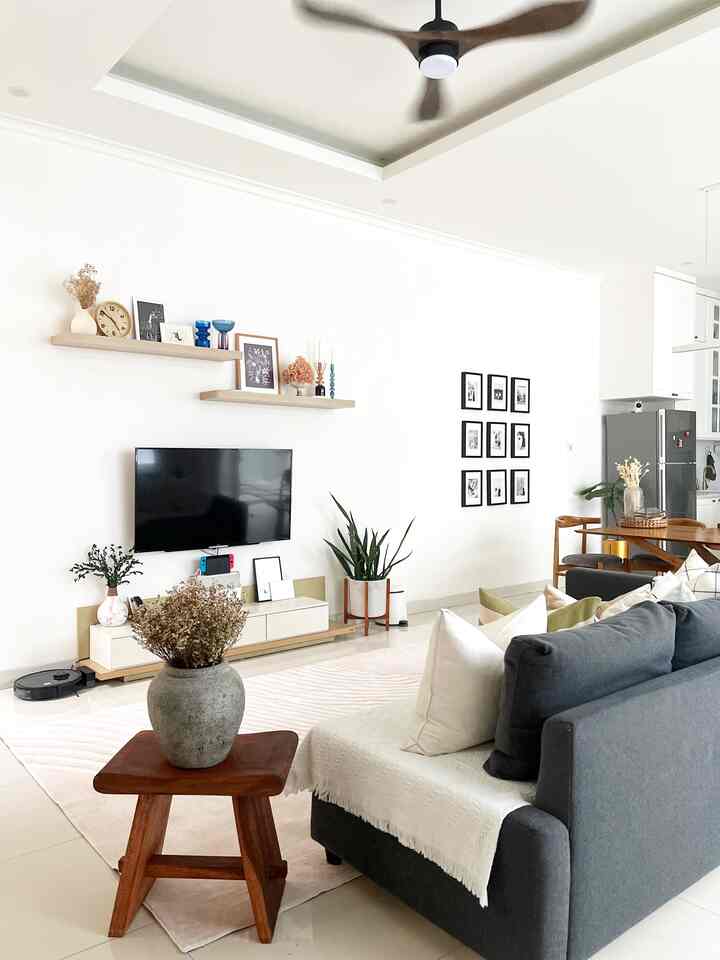 Natural interior of open-plan living room and kitchen featuring white walls, wood-toned furniture, and a gray sofa
