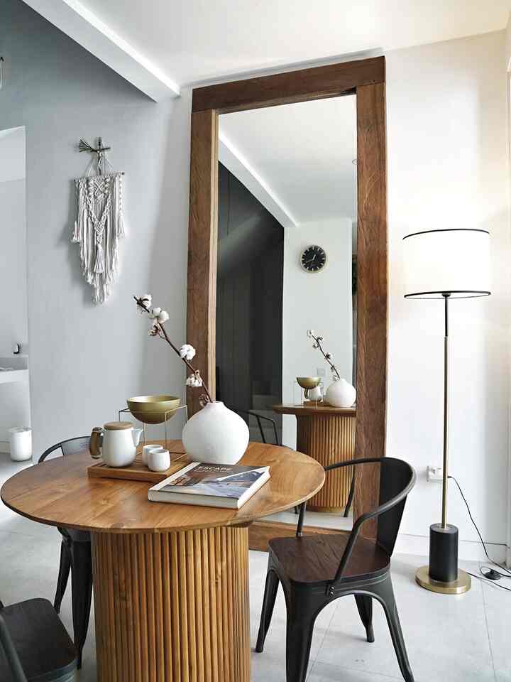 White and wood tone dining room featuring a round dining table, large mirror, and gold accents in a modern natural style
